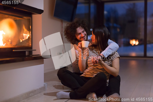 Image of happy multiethnic couple sitting in front of fireplace