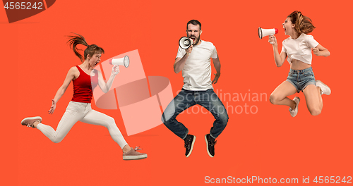 Image of Beautiful young man and woman jumping with megaphone isolated over red background