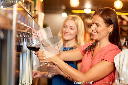 Image of happy women pouring wine from dispenser at bar