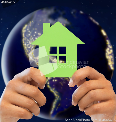 Image of hands holding green house over earth in space