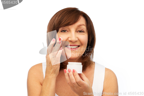 Image of smiling senior woman applying cream to her face