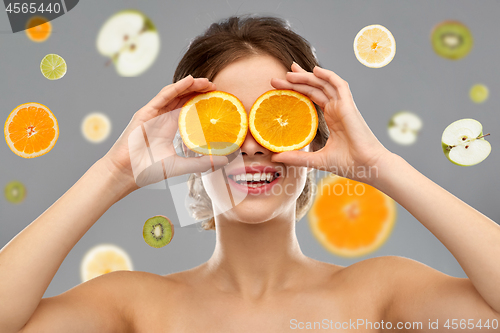 Image of smiling woman with oranges on eyes over fruits