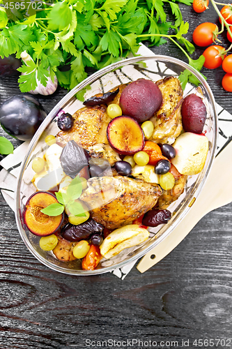 Image of Chicken with fruits and tomatoes in glass pan on dark board top