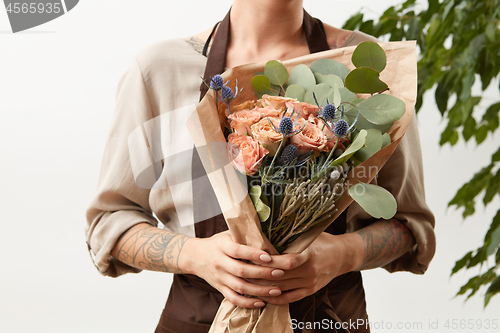 Image of Woman\'s hands with tattoo hold flower roses bouquet for congratulation on a light background, place for text. Greeting card concept.