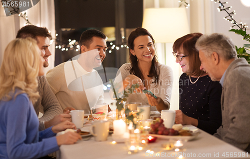 Image of happy family with smartphone at tea party at home