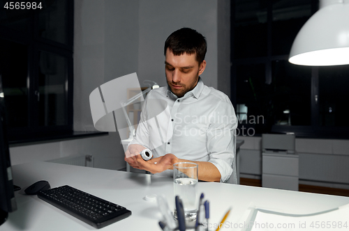 Image of businessman taking medicine pill at night office