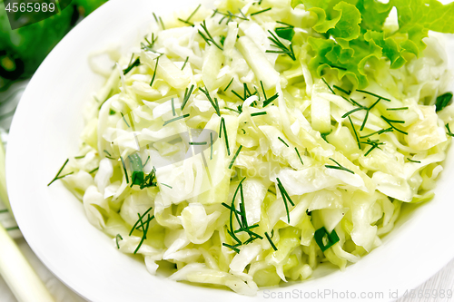 Image of Salad of cabbage and cucumber in plate on wooden board