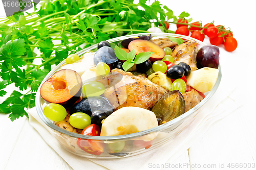 Image of Chicken with fruits and tomatoes in pan on light wooden board