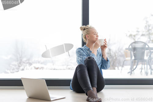 Image of woman drinking coffee and using laptop at home