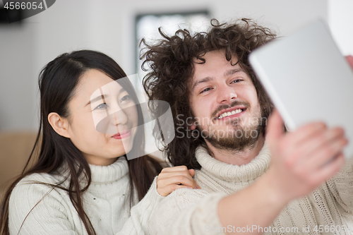 Image of multiethnic couple using tablet computer in front of fireplace