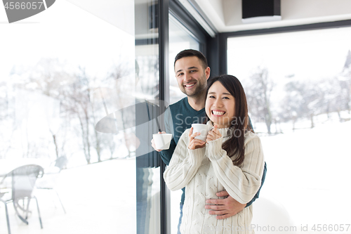 Image of multiethnic couple enjoying morning coffee by the window