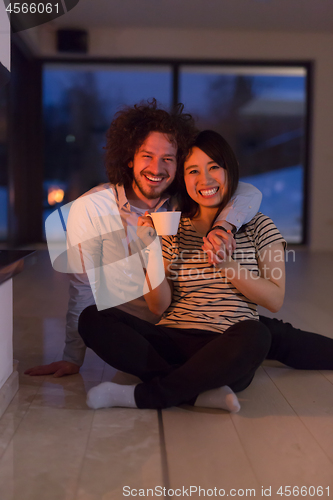 Image of happy multiethnic couple sitting in front of fireplace