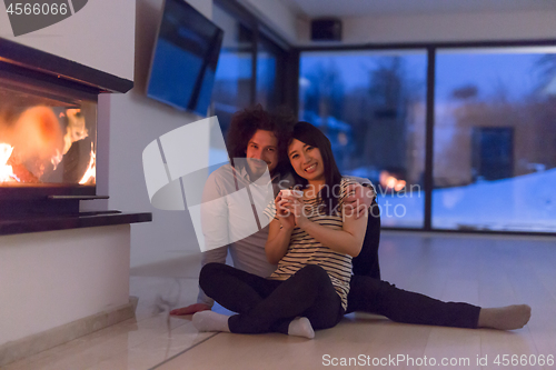 Image of happy multiethnic couple sitting in front of fireplace