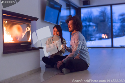 Image of happy multiethnic couple sitting in front of fireplace