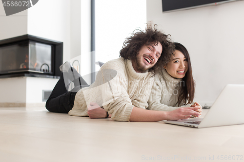 Image of young multiethnic couple using a laptop on the floor