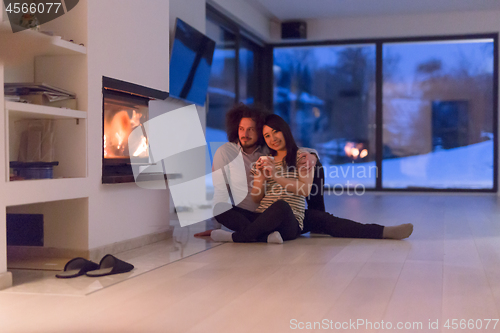 Image of happy multiethnic couple sitting in front of fireplace