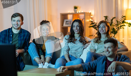 Image of happy friends watching tv at home in evening