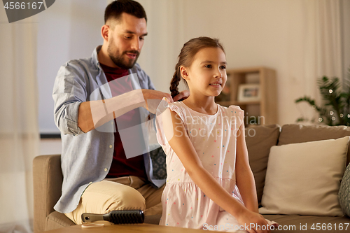 Image of father braiding daughter hair at home