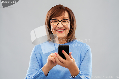 Image of smiling senior woman in glasses using smartphone