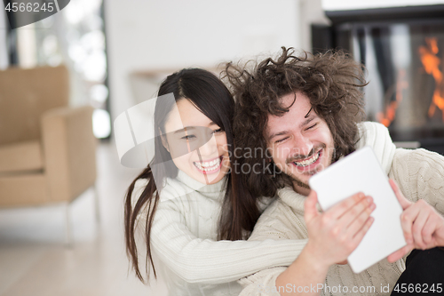 Image of multiethnic couple using tablet computer in front of fireplace