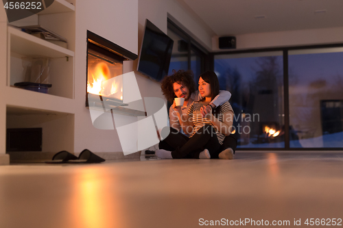 Image of happy multiethnic couple sitting in front of fireplace