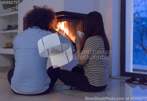 Image of happy multiethnic couple sitting in front of fireplace