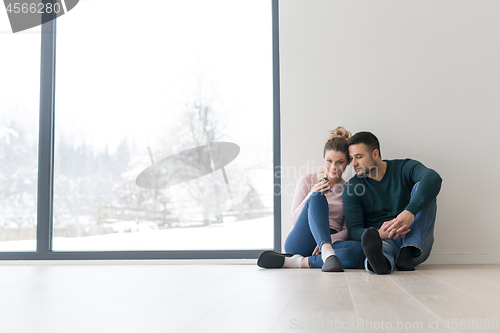 Image of young couple sitting on the floor near window at home