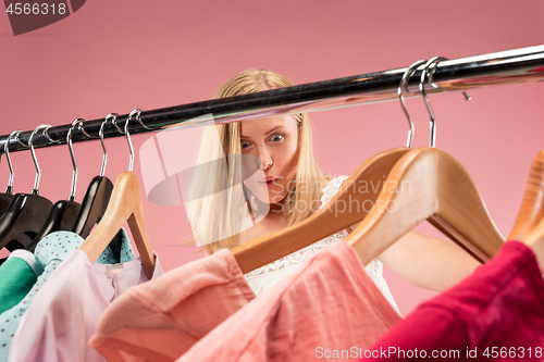 Image of The young unhappy pretty girl looking at dresses and try on it while choosing at shop