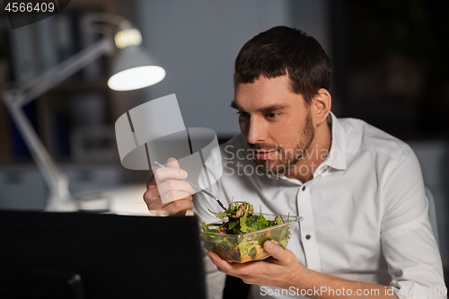 Image of businessman with computer eating at night office