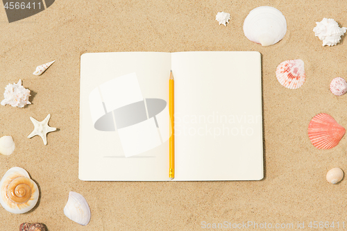 Image of notebook with pencil and seashells on beach sand