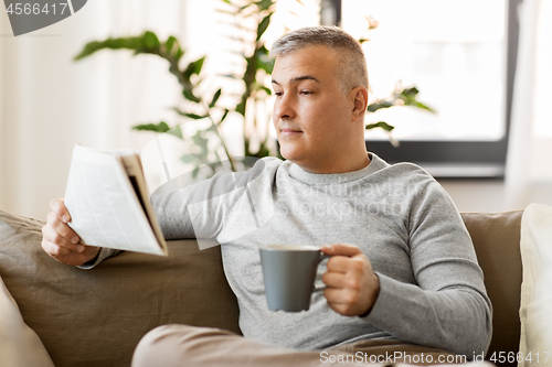 Image of man reading newspaper and drinking coffee at home