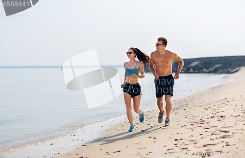 Image of couple in sports clothes running along on beach