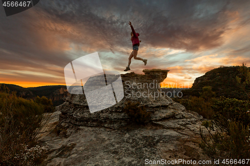 Image of Active woman jumping on mountain cliffs at sunset