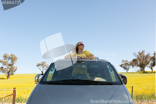 Image of Beautiful woman standing in the sunroof of her car on a road trip to countryside