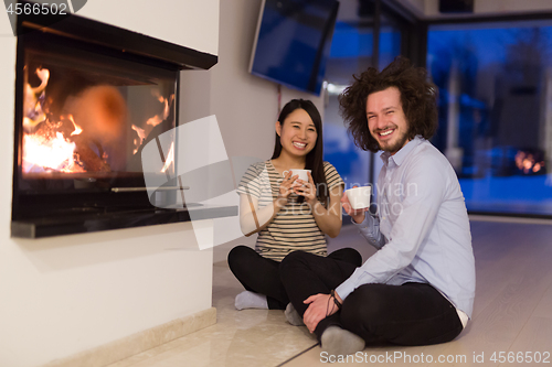 Image of happy multiethnic couple sitting in front of fireplace