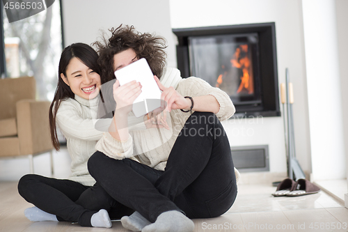 Image of multiethnic couple using tablet computer in front of fireplace