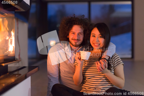 Image of happy multiethnic couple sitting in front of fireplace