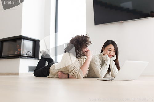 Image of young multiethnic couple using a laptop on the floor