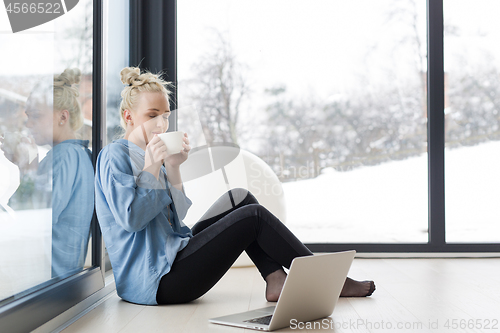 Image of woman drinking coffee and using laptop at home