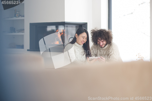 Image of multiethnic couple using tablet computer in front of fireplace