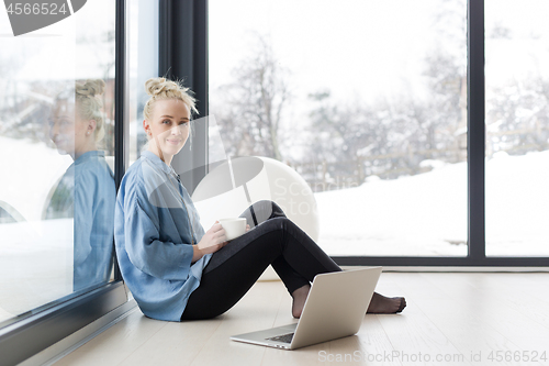 Image of woman drinking coffee and using laptop at home