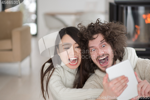 Image of multiethnic couple using tablet computer in front of fireplace