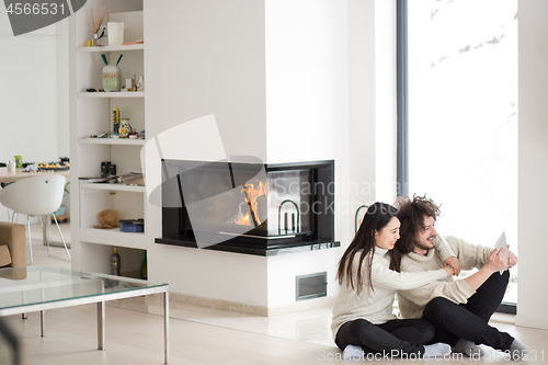 Image of multiethnic couple using tablet computer in front of fireplace