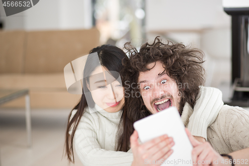 Image of multiethnic couple using tablet computer in front of fireplace