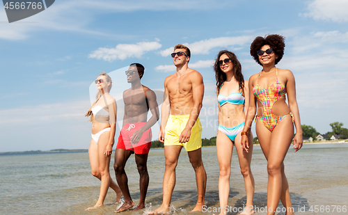 Image of happy friends walking along summer beach