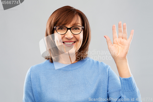 Image of portrait of senior woman in glasses waving hand