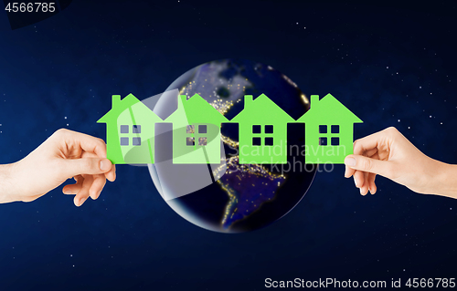Image of hands holding green house over earth in space