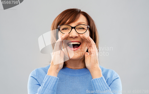 Image of senior woman in glasses calling over grey