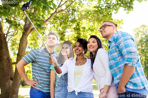 Image of happy friends taking photo by selfie stick at park