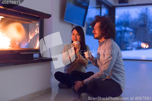 Image of happy multiethnic couple sitting in front of fireplace